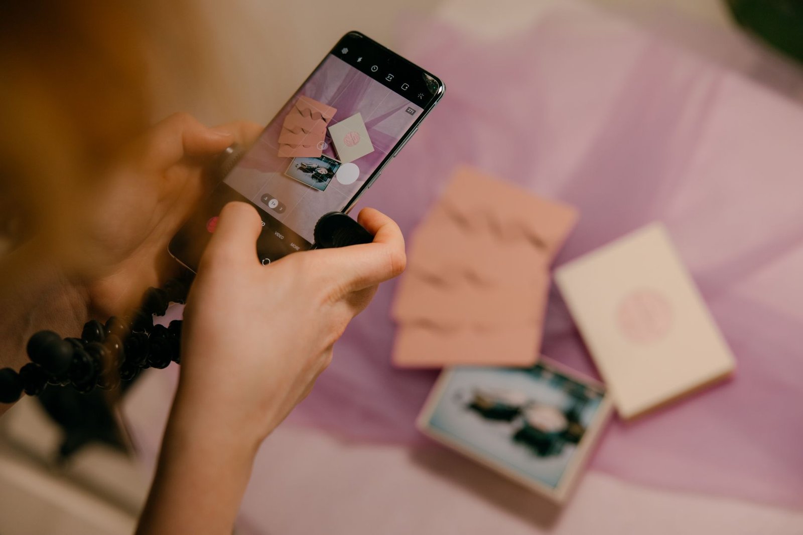 Close-up of hands photographing pink stationery with a smartphone on a soft background.